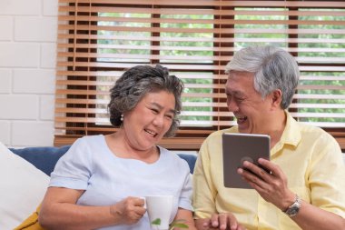 Masa bilgisayarve içki kahve evde oturma odasında kanepede oturan kullanarak Asyalı yaşlı çift.kıdemli teknoloji lfiestyle.aging evde kavramı ile.