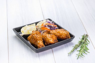 Kızarmış tavuk kanadı ve masa örtüsünün üzerinde salata.