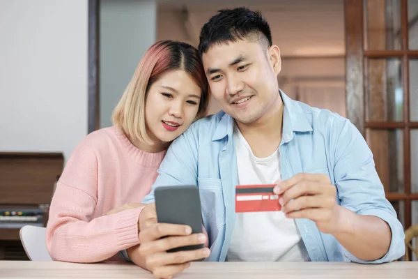 Asian couple use mobile phone shopping online with credit card together in living room at home.couple in home concept