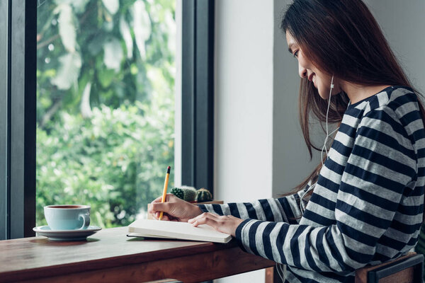 asian woman write plan to do list on notebook white listening music at home in quarantine time
