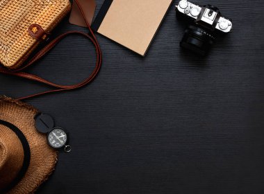 Yaz seyahati düz aksesuar seti. Şapka, sarı hasır çanta, kamera ve defter siyah ahşap masa üzerinde. Sağ tarafta kopya alanı bırakın.