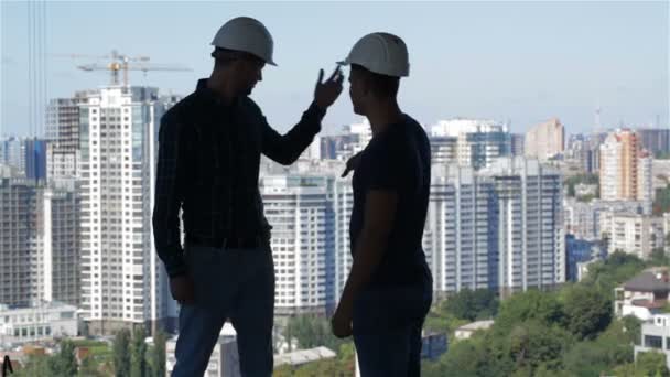 Два строителя смотрят на ландшафт высоких зданий — стоковое видео