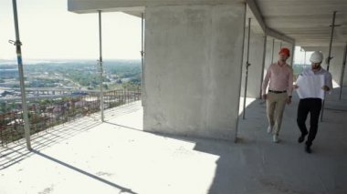 İnşaat aşamasındaki binada yürüyen iki erkek inşaatçı