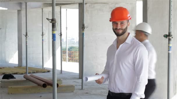 Male builder holds set of plans of building under construction — Stock Video