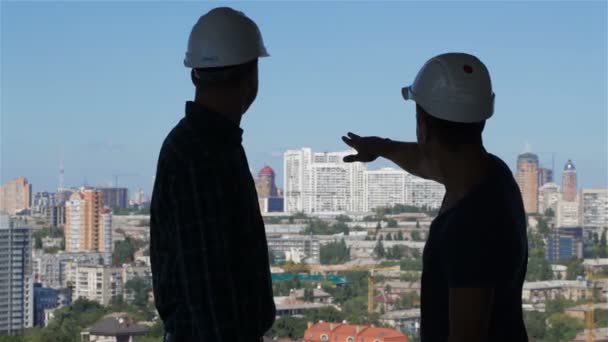 Builder aponta sua mão para o complexo de edifícios altos — Vídeo de Stock