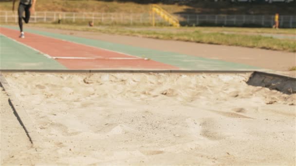 Мужской атлет совершает прыжок в длину на стадионе — стоковое видео