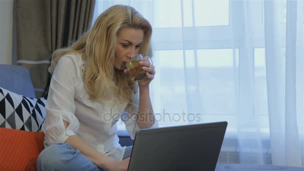 Mujer bebe té cerca de la computadora portátil en casa — Vídeo de stock
