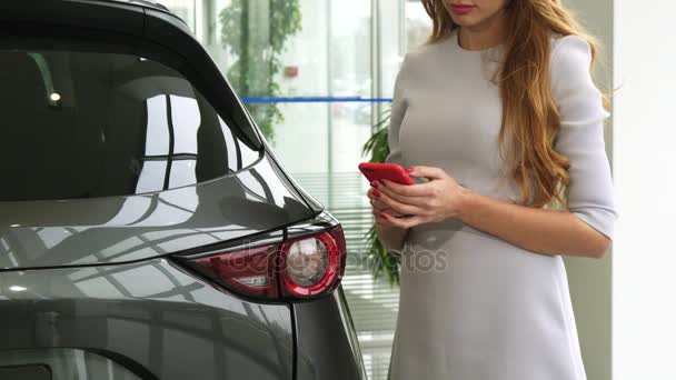 Recorte de una mujer usando un teléfono inteligente en el concesionario de automóviles — Vídeo de stock