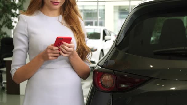 Recortado disparo de una mujer alegre usando el teléfono inteligente de pie cerca de su coche — Vídeo de stock