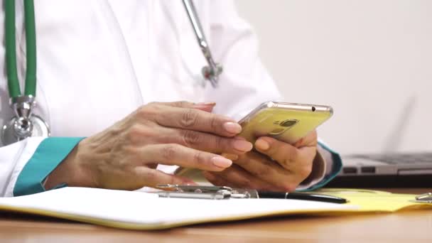 Cropped close up of a female doctor using smart phone writing notes — Stock Video