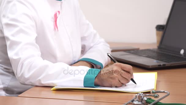 女医の仕事で彼女のラップトップを使用してメモを書くのショットをトリミング — ストック動画