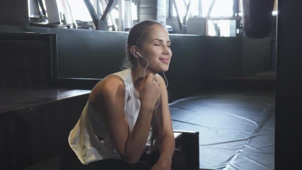 Fröhliche sexy junge Fitness-Frau genießt Musik hören in der Turnhalle — Stockvideo