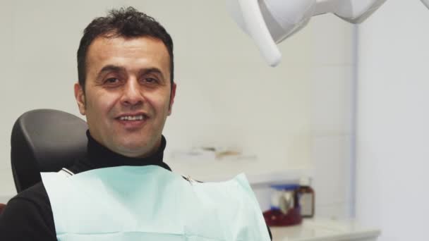 Happy mature man smiling holding an apple sitting in a dental chair — Stock Video