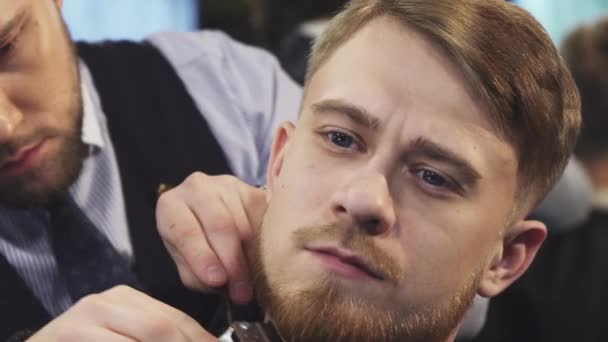 Nahaufnahme eines professionellen Friseurs, der einem jungen Mann den Bart schneidet — Stockvideo