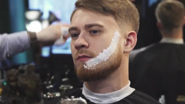 Peluquero aplicando crema de afeitar en la barba de su cliente — Vídeos de Stock