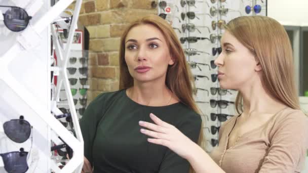 Красиві щасливі молоді друзі-жінки, які вибирають окуляри в окуліста — стокове відео