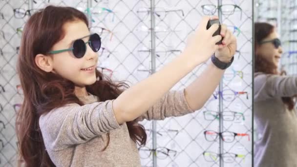Aranyos kis boldog lány vesz selfies, a szemüveg bolt — Stock videók