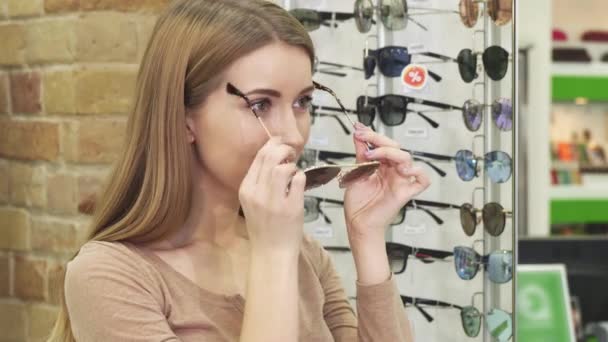 Fröhliche schöne Frau probiert Sonnenbrille im Optikerladen aus — Stockvideo