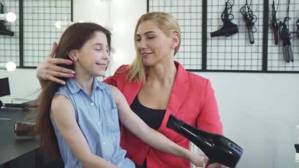 Όμορφη γυναίκα στέγνωμα μαλλιών της κόρης της με στεγνωτήρα στο σαλόνι ομορφιάς — Αρχείο Βίντεο