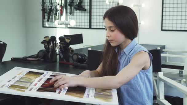 Menina bonita examinando gráfico de cores de tintura de cabelo no salão de beleza — Vídeo de Stock