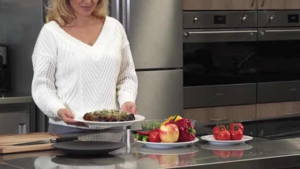 美丽成熟的女人微笑着用盘子摆在烹饪后的镜头 — 图库视频影像