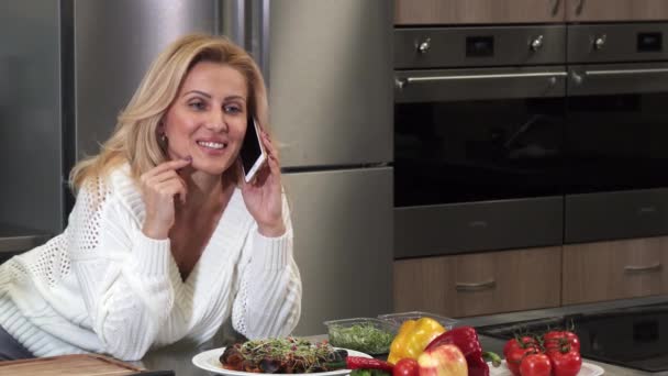 Εντυπωσιακή χαρούμενος ώριμη γυναίκα που μιλάει στο τηλέφωνο στην κουζίνα — Αρχείο Βίντεο