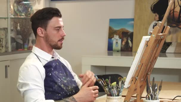 Ung skäggiga manliga artist att undersöka hans konstverk tänkande arbetar på hans studio — Stockvideo
