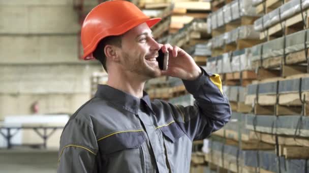 Trabalhador da fábrica feliz em um chapéu duro sorrindo falando ao telefone — Vídeo de Stock