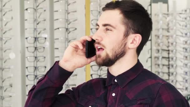 Joven alegre hablando por teléfono en la tienda de óptica — Vídeo de stock