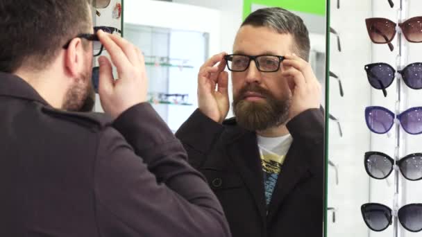Älterer Mann probiert neue Brille vor dem Spiegel im Geschäft an — Stockvideo