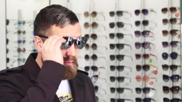 Зрілий чоловік пробує сонцезахисні окуляри в магазині оптики — стокове відео