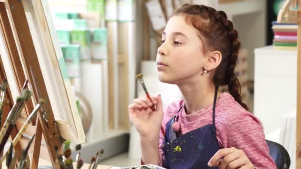 Linda niña mostrando pulgares hacia arriba mientras que la pintura de un cuadro en la clase de arte — Vídeo de stock