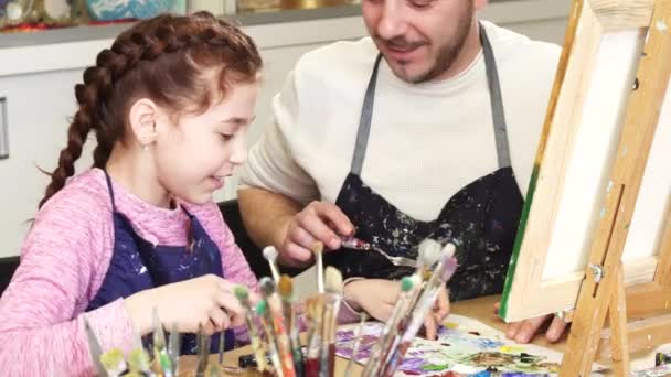 Beskuren bild av en söt liten flicka leende talar till hennes pappa blanda färger på konst klass — Stockvideo