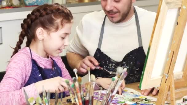 Colpo ritagliato di una ragazza carina sorridente parlando con suo padre mescolando vernici a lezione d'arte — Video Stock