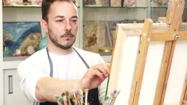 Зріла чоловіча художниця працює над картиною у своїй художній студії — стокове відео