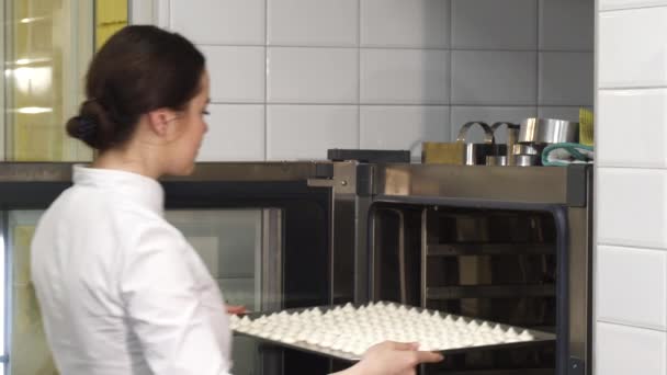 Joven hermosa pastelera poniendo merengues en el horno — Vídeos de Stock