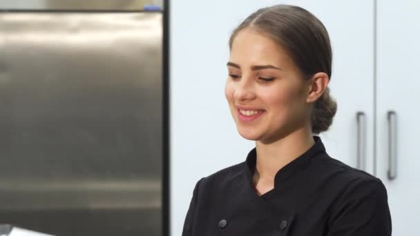 Ελκυστική γυναίκα baker χαμογελά στη φωτογραφική μηχανή, κρατώντας ένα τόξο από ζαχαρωτά — Αρχείο Βίντεο