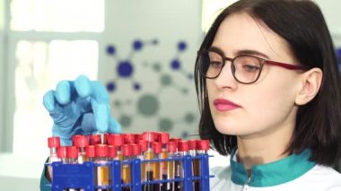 Genç bir kadın araştırmacı test tüpleri ile kan örnekleri inceleyerek yakın çekim