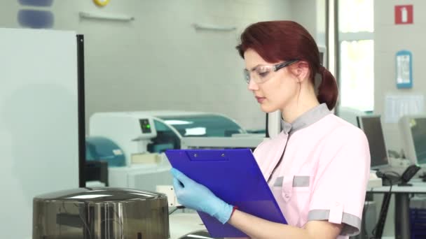 Νεαρή γυναίκα επιστήμονας κρατώντας σημειώσεις στο σύγχρονο εργαστήριο — Αρχείο Βίντεο