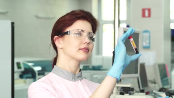 Young female biologist examining two test tubes with blood — Stock Video