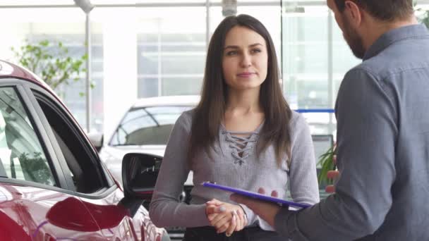 Jonge vrouw in gesprek met de verkoper bij het autobedrijf — Stockvideo