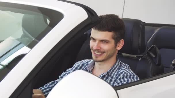 Красивый счастливый молодой водитель с ключами от машины, сидящий в машине — стоковое видео