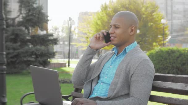 Fešák africký americký podnikatel pomocí chytrého telefonu a notebooku venku — Stock video