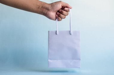 Eller mavi arkaplana karşı beyaz kağıt torba tutar