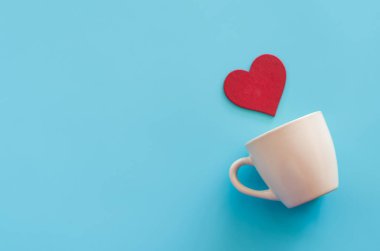 Boş kahve fincanı ve kalp şeklinde ahşap bir parça mavi arka planda.