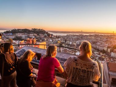 LISBON, PORTUGAL - NOVEMBER 19, 2017: Tourists at Belvedere of Our Lady of Hill viewpoint looking at cityscape of Lisbon at sunset clipart