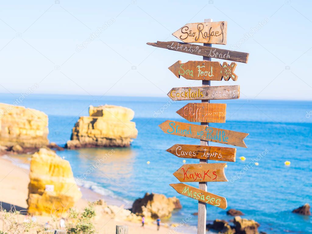 close-up photo of wooden signs board at beautiful rocky Sao Rafael beach with clean blue water in Algarve region, Portugal. 