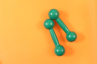 Turuncu zemin üzerine yeşil dumbell ağırlık