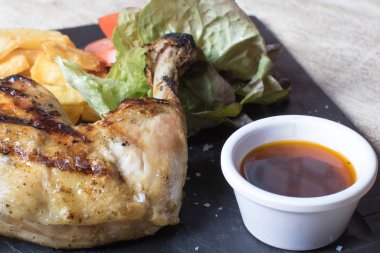 Patatesli tavuk budu, salata, domates ve siyah taş tabakta sos.