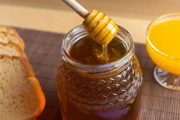 天然の蜂蜜 オレンジジュース 素朴なパンと蜂蜜のスプーンでまだ生きている蜂蜜瓶に落ちる — ストック写真